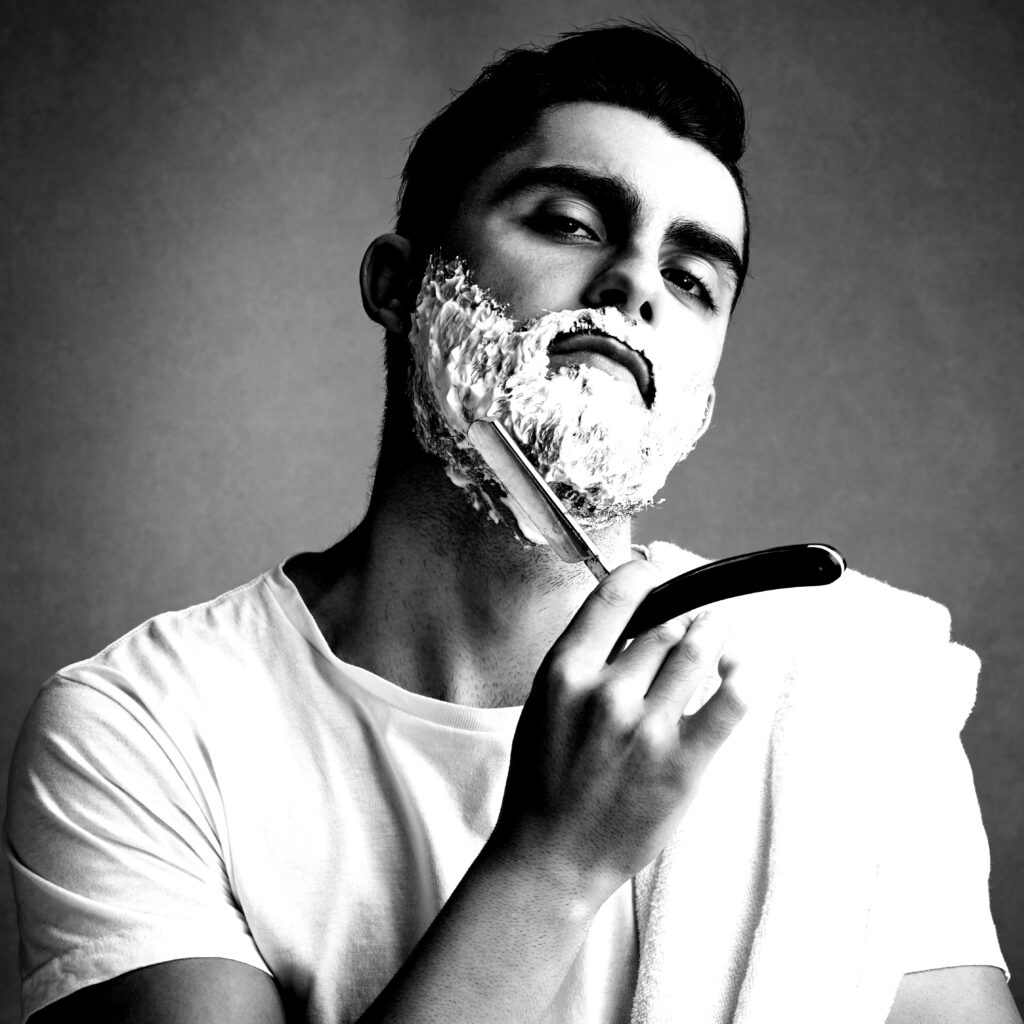 Un homme se rase avec de la mousse et un rasoir