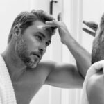 Un homme applique un soin sur son visage devant un miroir