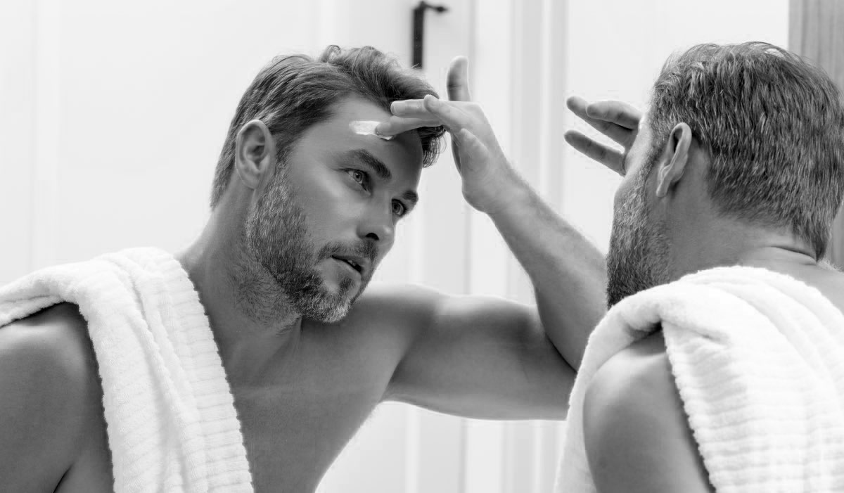 homme qui se passe de la crème hydratante pour homme devant un miroir